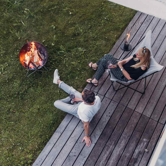 Vue du dessus de 2 personnes profitant de la chaleur du Brasero Hofats Bowl barbecue incliné vers eux