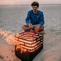 Homme installé devant le Brasero corten Cube Höfats avec des flammes