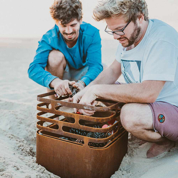 Allumage du Brasero corten Cube Höfats avec des pommes de pin sur la plage