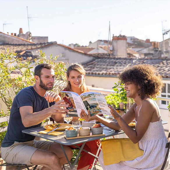 Femme montrant à ses amis 1 recette dans le livre Cuisiner à la plancha toute l'année par ENO et Delphine Lebrun