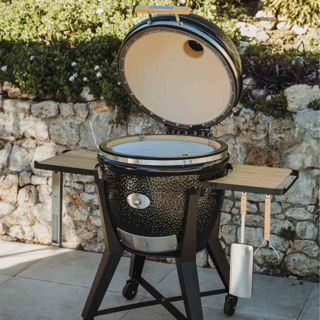 Photo d'ambiance du kamado TWO.66 noir sur chariot avec son couvercle ouvert et ses tablettes en bois de bambou Photo d'ambiance du kamado TWO.66 noir sur chariot avec son couvercle ouvert et ses tablettes en bois de bambou