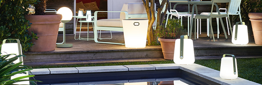 Différentes lampes Fermob allumées installées sur une terrasse et près d'une piscine