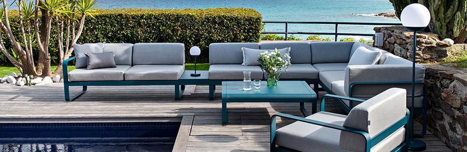 Terrasse avec canapés et sièges en bord de mer avec les lampes Fermob bleues