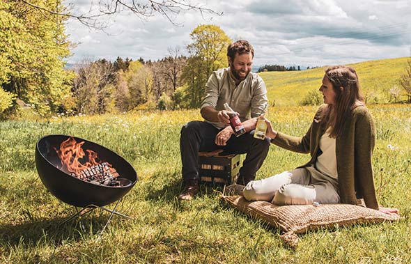 Brasero barbecue Bowl Hofats posé sur l'herbe près de 2 personnes