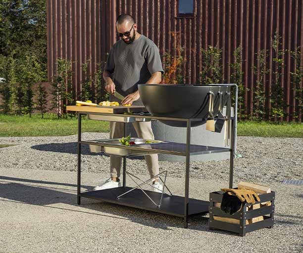 Préparation du repas sur la cuisine extérieure Fire Kitchen Höfats avec Bowl 70 dans un jardin