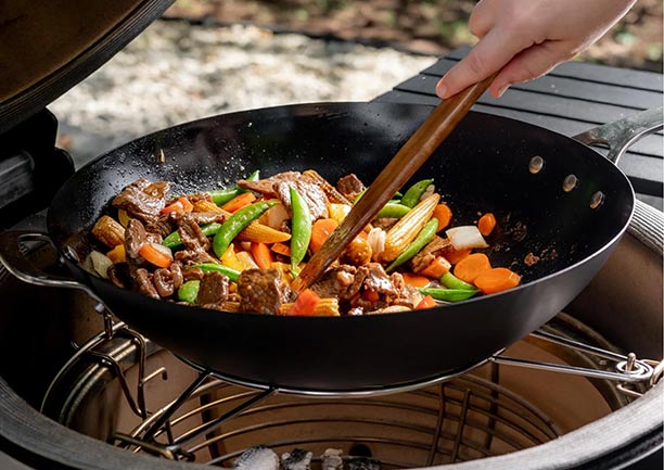 Wok en acier au carbone Karbon Steel™ de Kamado Joe posé sur le support à accessoires d'un gril kamado