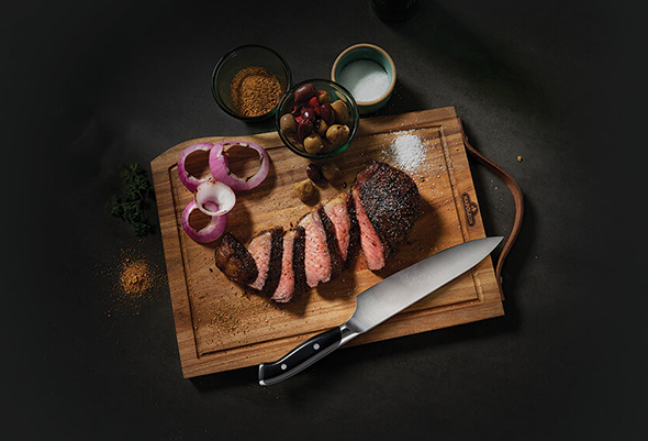 Découpe d'une viande et d'un oignon rouge sur la planche en acacia avec le couteau de chef inox 20 cm - Napoleon