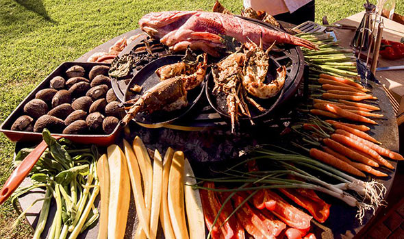 Nombreux légumes et morceaux de viandes en cuisson sur la plaque du brasero OFYR