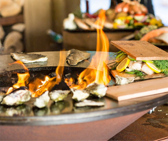 Cuissons d'huitres, poissons et saumons sur planche de bois installé sur le brasero OFYR