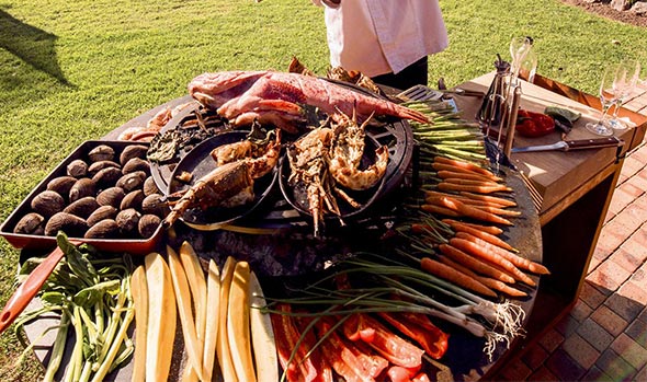 Nombreux légumes et morceaux de viandes en cuisson sur la plaque du brasero OFYR