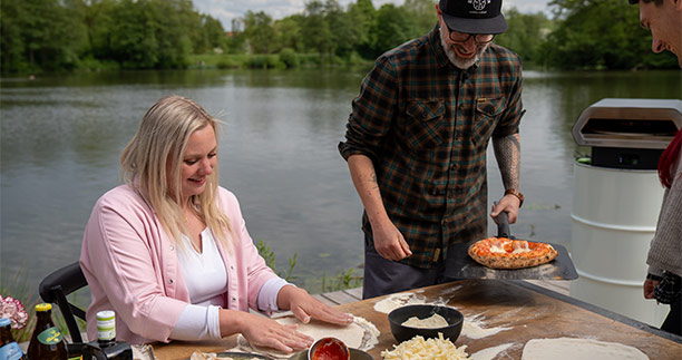 Femme qui prépare une pizza et homme qui tient la pelle à pizza en aluminium Outdoorchef