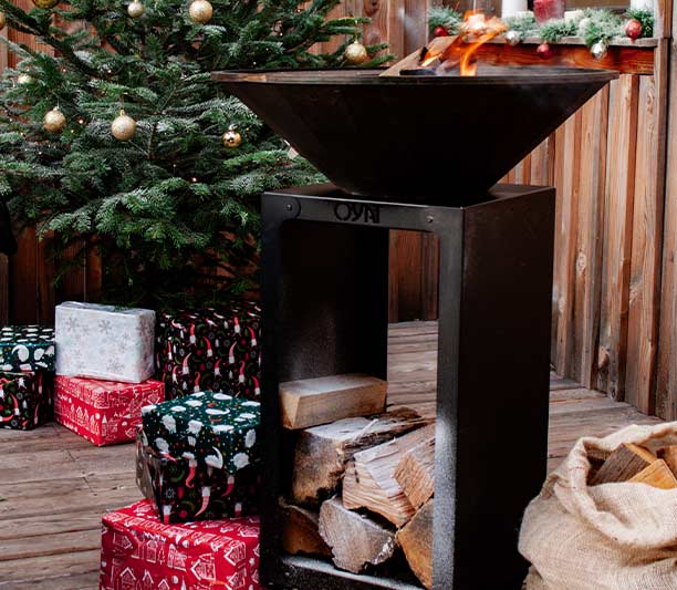 brasero B.B.O 58 en acier noir Oyat sur une terrasse avec un sapin et des cadeaux de noël