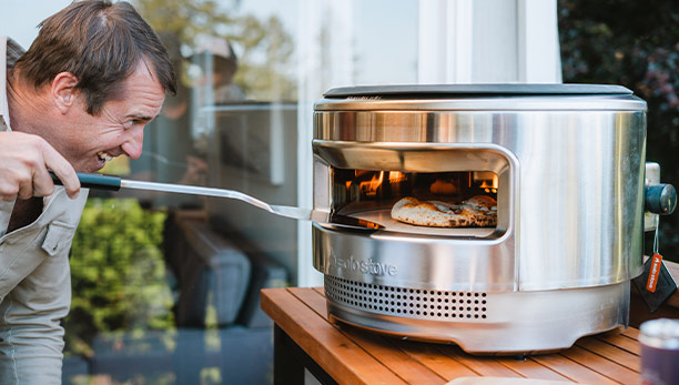 Homme utilisant la pelle en inox Solo Stove pour tourner une pizza