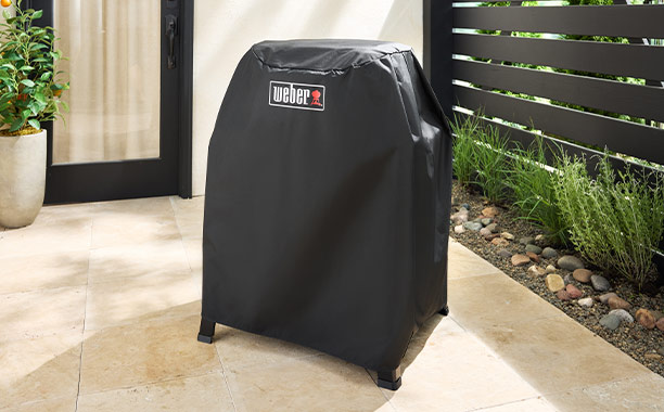 Barbecue électrique Weber Lumin sur stand avec sa housse exposé sur une terrasse