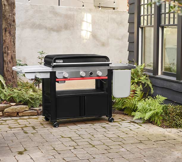 Plancha gaz sur chariot Weber Slate 76 cm avec le couvercle fermé sur une terrasse